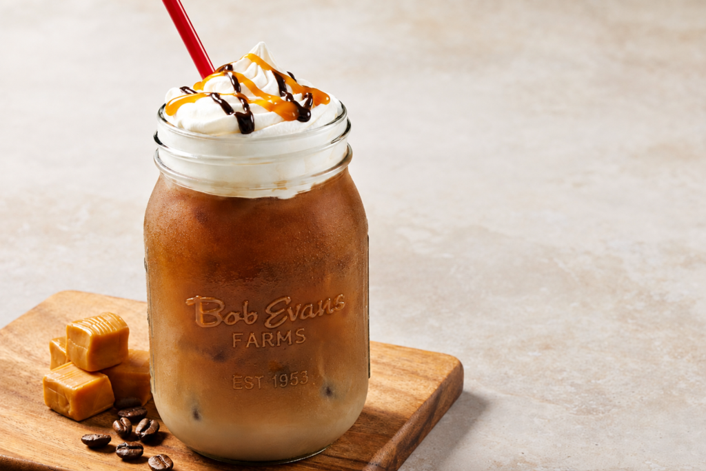 Iced caramel mocha coffee topped with whipped cream, chocolate and caramel drizzle, served cold in a glass mason jar.