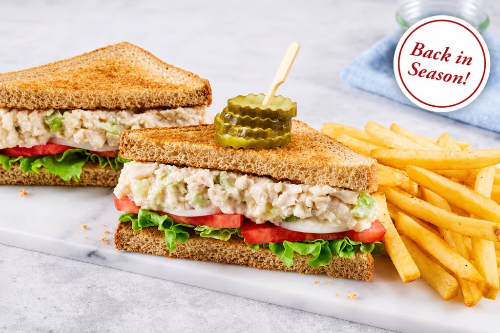 Chicken salad sandwich with creamy chicken salad, crisp lettuce, tomato and onion on toasted wheat bread, topped with pickles and served with golden French fries.