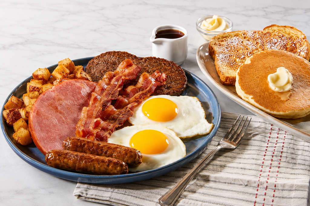 The Whole Hog breakfast platter with sunny-side-up eggs, crispy bacon, sausage links, sausage patties, ham and seasoned breakfast potatoes, served with pancakes, French toast, butter and syrup.